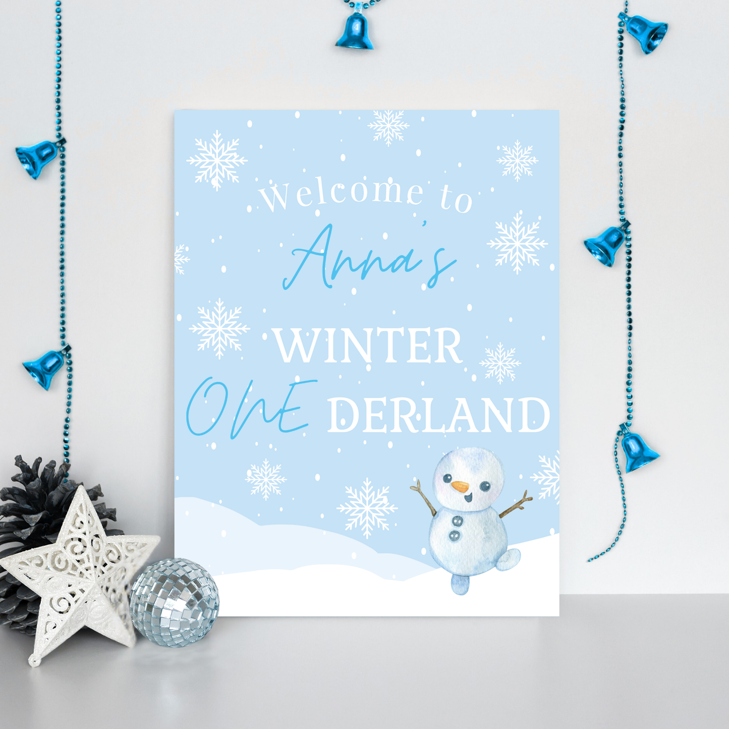 Decorative sign with a snowman and text 'Welcome to Anna's Winter One Derland' on a light blue background.